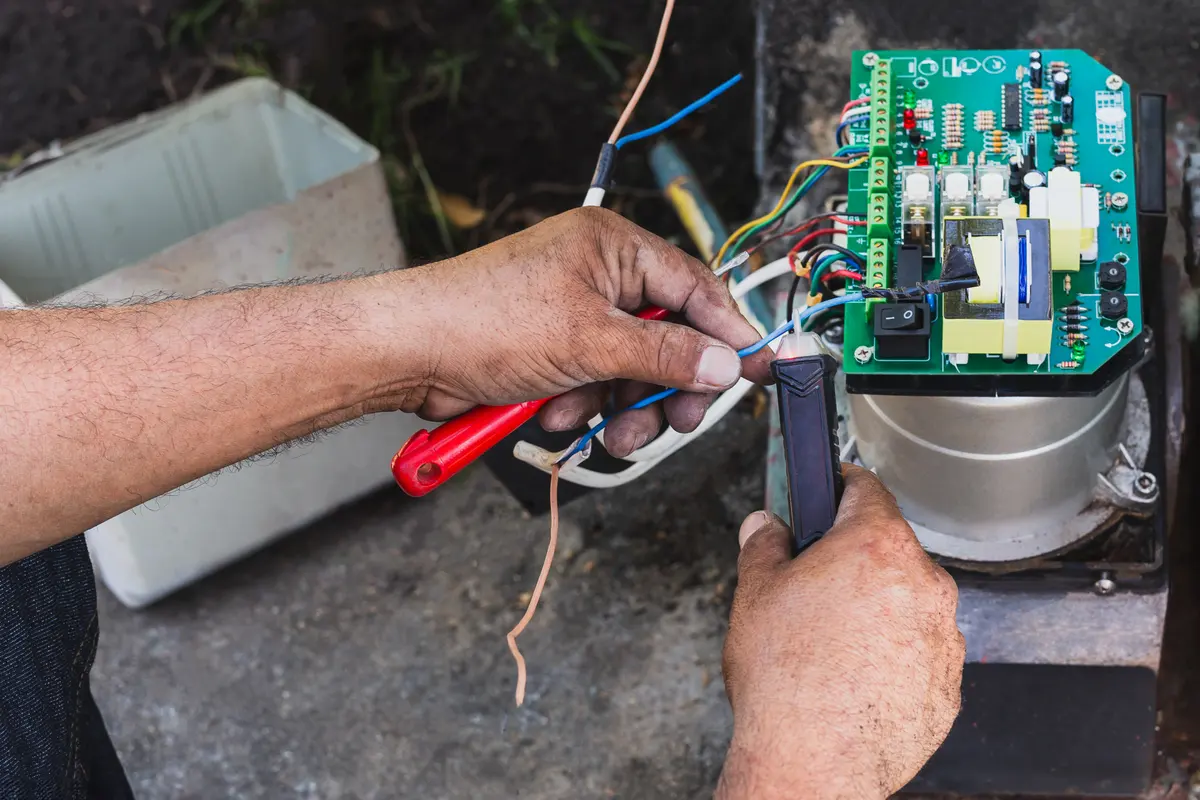 Mains d’un technicien raccordant un fil sur la carte électronique d’une motorisation de portail, coffret ouvert