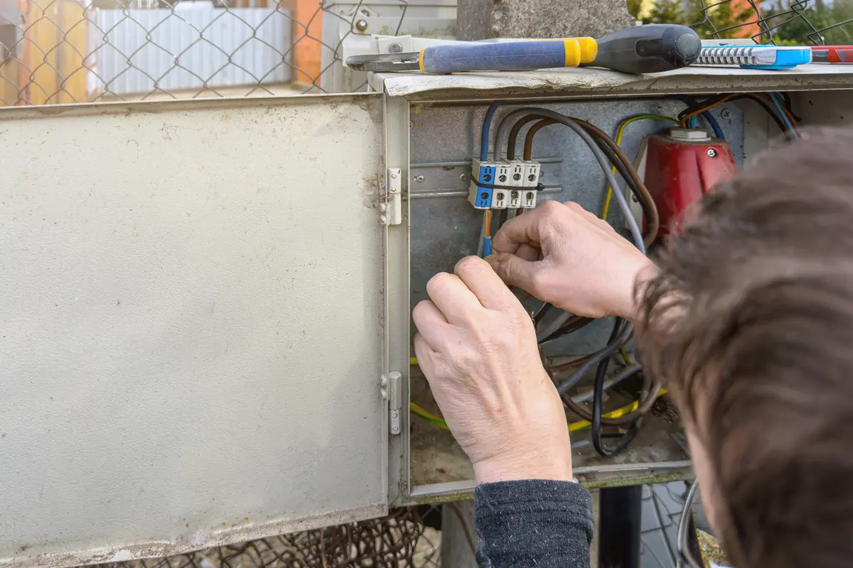 Technicien vérifiant le raccordement des câbles dans le coffret électrique extérieur d’un portail