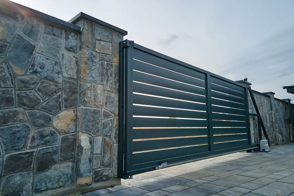 Portail coulissant en aluminium anthracite à lames, refoulé le long d’un mur en pierre, son bras de guidage visible au sol